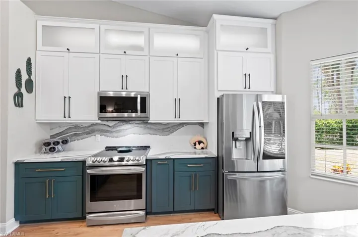 Kitchen featuring white cabinets, appliances with stainless steel finishes, glass insert cabinets, light stone counters, and vaulted ceiling