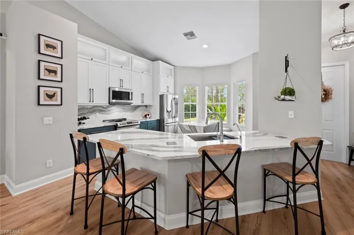 Kitchen featuring white cabinetry, light stone counters, stainless steel appliances, light wood-type flooring, and backsplash