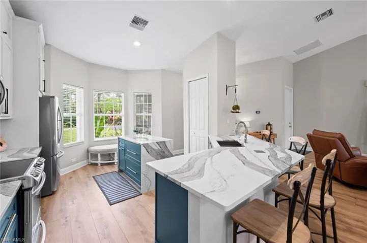 Kitchen featuring blue cabinetry, a kitchen bar, light stone counters, a kitchen island, and light wood-style floors