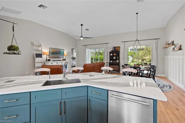 Kitchen featuring blue cabinetry, open floor plan, dishwasher, light stone counters, and light wood-type flooring