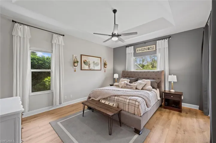 Bedroom with light wood-style floors, ceiling fan, and multiple windows
