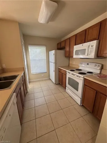 Kitchen featuring stove, light countertops, dishwashing machine, wood finish cabinets, and light tile patterned floors