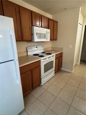 Kitchen with white appliances, wood finish cabinetry, light countertops, and light tile patterned flooring