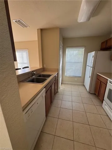Kitchen with dishwashing machine, stove, light countertops, light tile patterned flooring, and wood finish cabinets