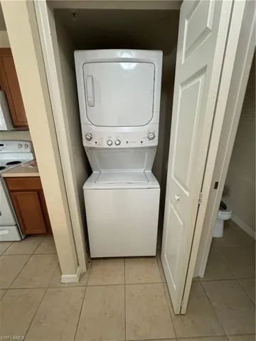 Laundry area with stacked washer and dryer and light tile patterned flooring