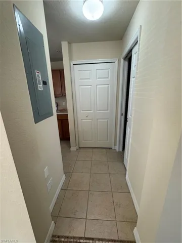 Hallway with a textured wall, electric panel, a textured ceiling, and light tile patterned flooring