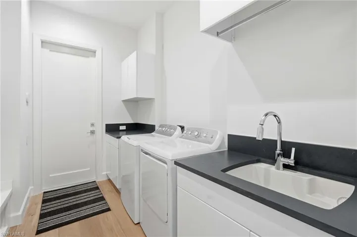 Functional utility room featuring light wood-finish flooring, white cabinetry, dark countertops, and a built-in utility sink with a chrome faucet