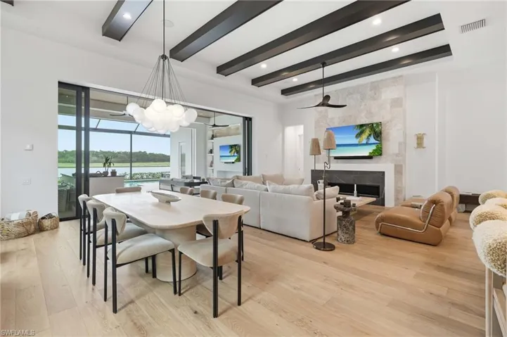 Expansive open-concept interior featuring light wood-finish flooring, a contemporary fireplace with a stone surround, and an exposed beam ceiling