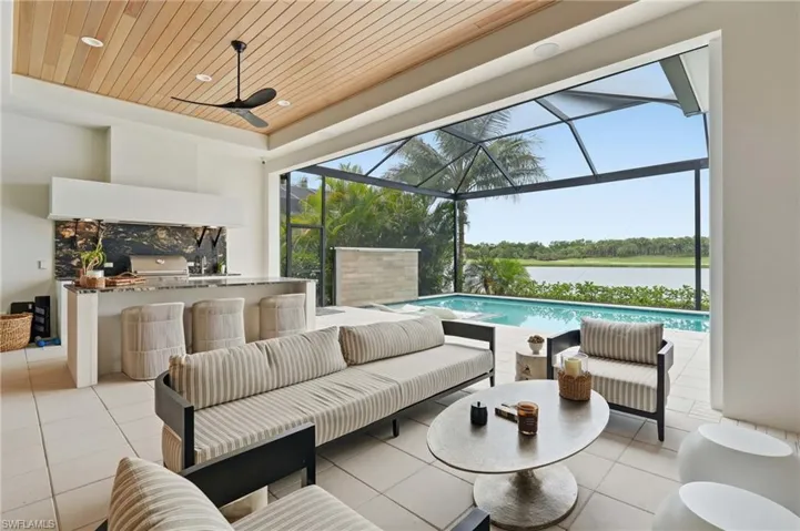 Expansive screened lanai featuring a swimming pool, outdoor kitchen with built-in grill, wood-finish ceiling, and tile flooring