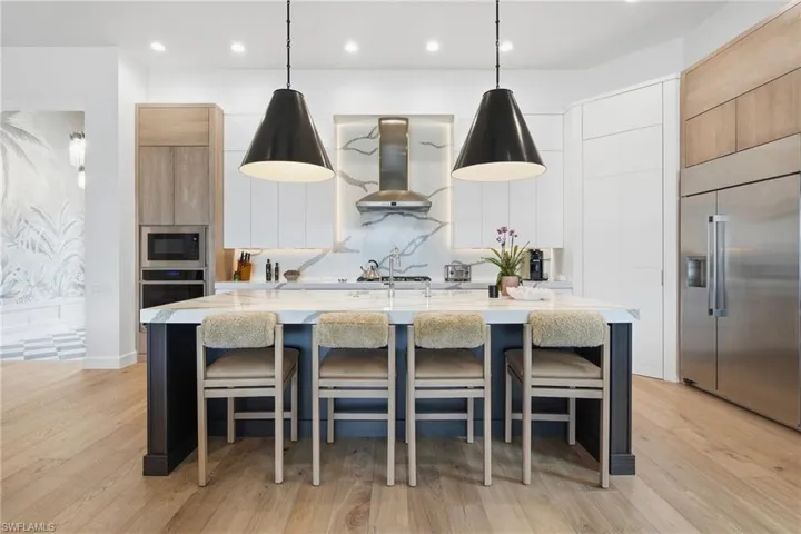 Gourmet kitchen featuring a large central island with seating, stainless steel appliances, wood-finish flooring, custom cabinetry, and a unique stone backsplash
