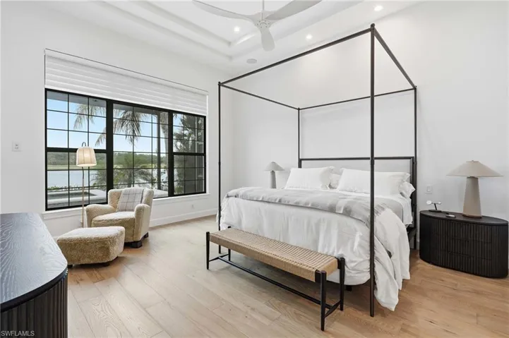 White walls with light wood-finish flooring, featuring a large window with black grilles, recessed lighting, and a tray ceiling