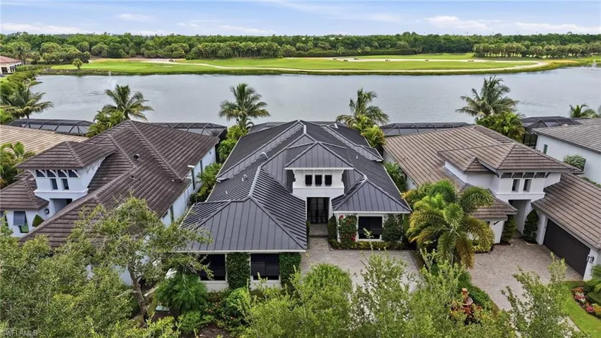 Contemporary home featuring a metal seam roof, lush landscaping, and a paver driveway