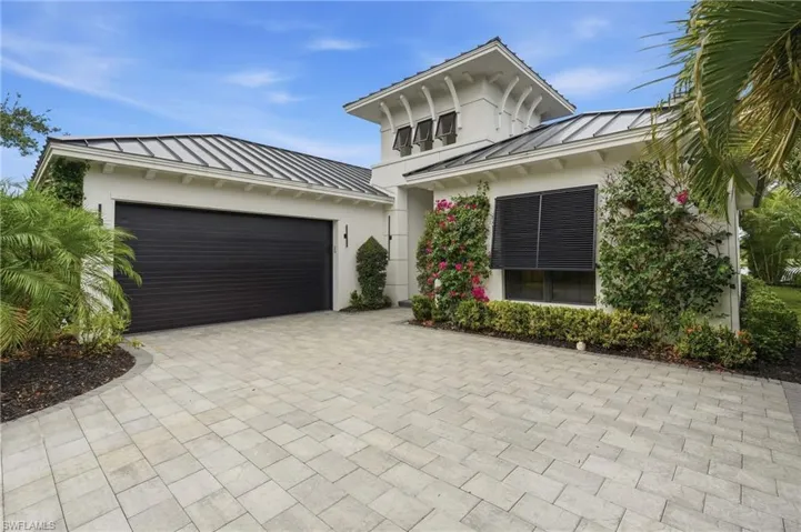 Contemporary exterior featuring a white stucco finish, a black metal roof, a black paneled garage door, a paved driveway, and established perimeter landscaping