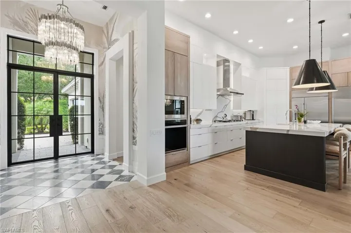 Open-concept kitchen and entryway featuring a crystal chandelier, checkered tile flooring, light wood-finish flooring, a kitchen island with seating, and stainless steel appliances