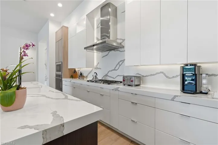 Modern kitchen featuring a waterfall-edge island, white slab cabinetry, integrated stainless steel appliances, a gas cooktop, and a matching backsplash