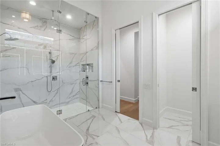 Spacious bathroom featuring a frameless glass shower enclosure with a rain shower head, a separate handheld shower fixture, and recessed shelving