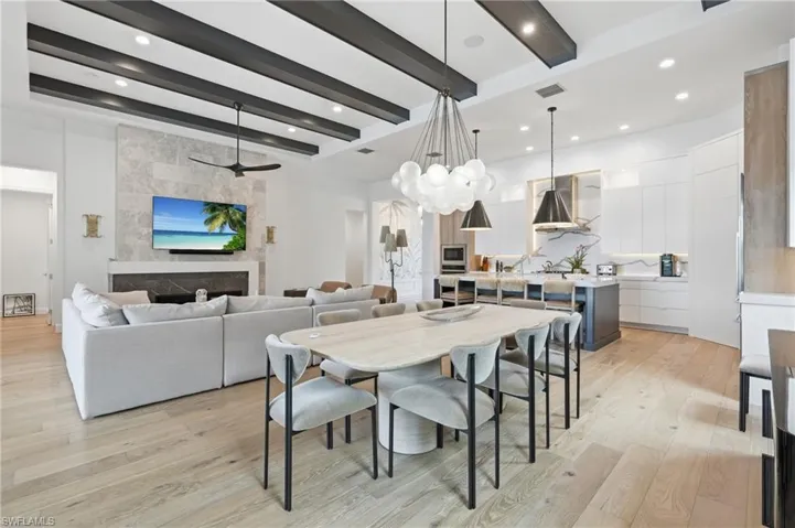 Open-concept living space with light wood-finish flooring, a contemporary kitchen featuring white cabinetry and a contrasting dark island, and a living area with a stone-clad fireplace