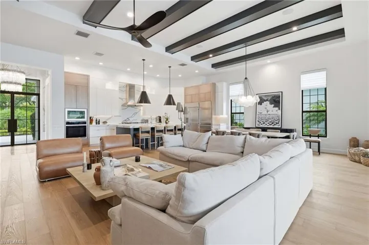 Spacious great room featuring wood-finish flooring, high ceilings with exposed beams, and contemporary lighting fixtures