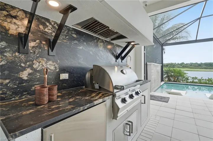 Outdoor kitchen featuring a built-in stainless steel grill, under-counter refrigeration, and dark patterned countertops