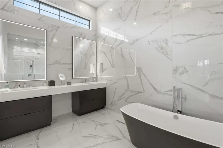 Spacious bathroom featuring large format marble-look tile, a freestanding soaking tub with floor-mounted fixtures, and a dual vanity with undermount sinks