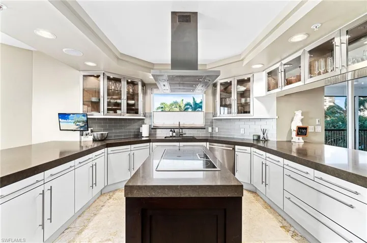 Kitchen featuring stainless steel dishwasher, island exhaust hood, white cabinetry, and sink