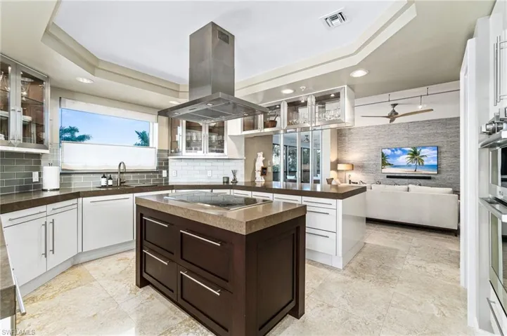 Kitchen featuring ceiling fan, island range hood, a center island, a tray ceiling, and stainless steel stovetop