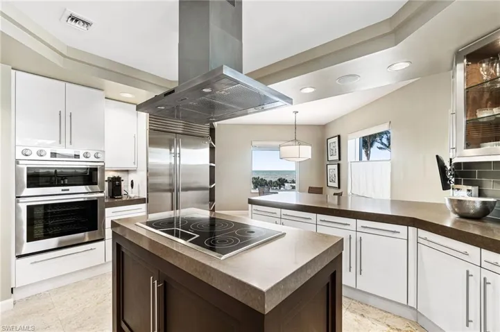 Kitchen with white cabinets, hanging light fixtures, tasteful backsplash, island range hood, and stainless steel appliances