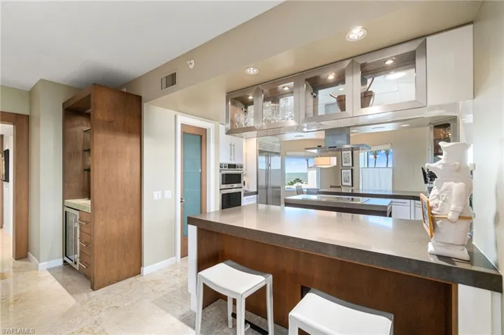 Kitchen with white cabinets, kitchen peninsula, island range hood, appliances with stainless steel finishes, and a breakfast bar