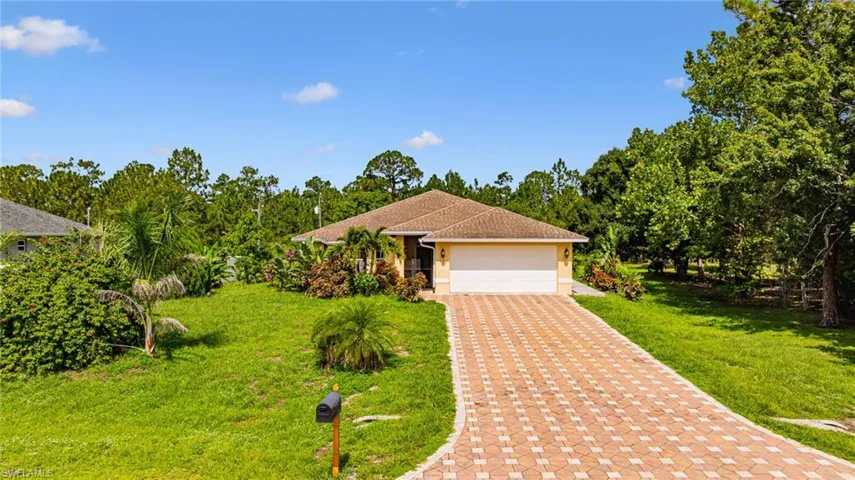 View of front of property featuring a front yard, a garage, stucco siding, decorative driveway, and view of scattered trees