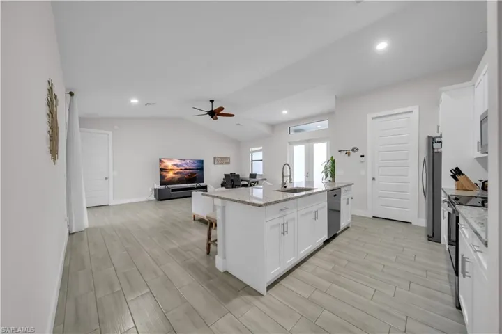 Kitchen with white cabinetry, open floor plan, a kitchen bar, light stone countertops, and appliances with stainless steel finishes