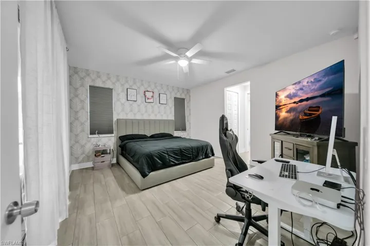 Bedroom featuring wallpapered walls, an accent wall, an office area, wood tiled floors, and ceiling fan