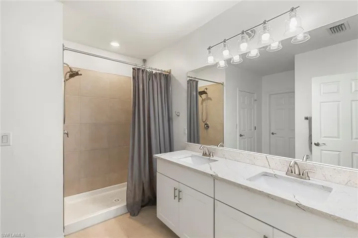 Bathroom featuring double vanity, a shower stall, and light tile patterned flooring