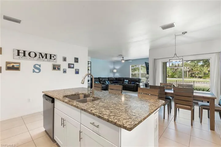 Kitchen featuring white cabinetry, open floor plan, ceiling fan, a center island with sink, and dark stone counters