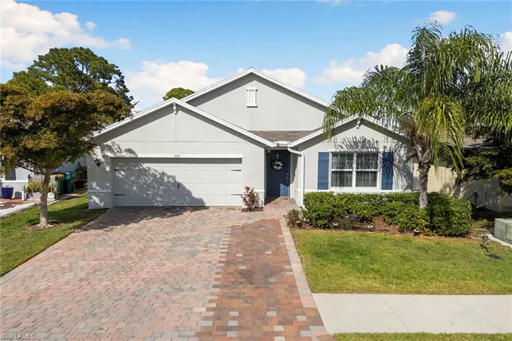 Ranch-style home with a front lawn, stucco siding, an attached garage, and decorative driveway