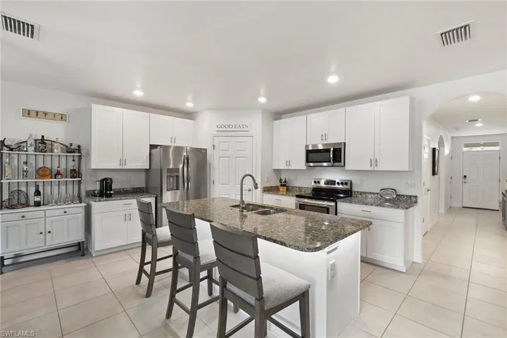 Kitchen featuring arched walkways, stainless steel appliances, a kitchen breakfast bar, white cabinets, and recessed lighting