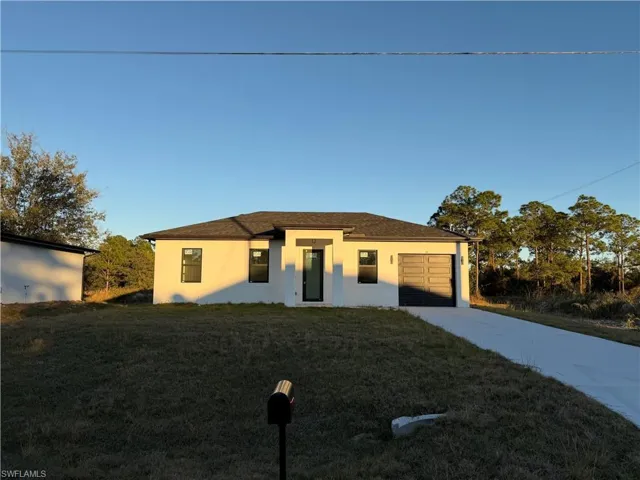 Prairie-style home featuring stucco siding, driveway, a front lawn, and a garage