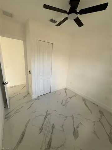 Unfurnished bedroom with light marble finish floors, a closet, and a ceiling fan