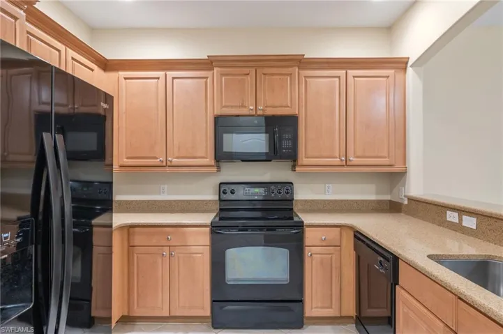 Kitchen featuring black appliances, light stone counters, and light tile patterned flooring