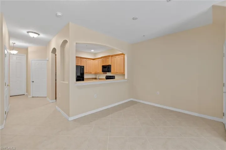 Kitchen with light tile patterned flooring, black appliances, light brown cabinets, arched walkways, and light countertops