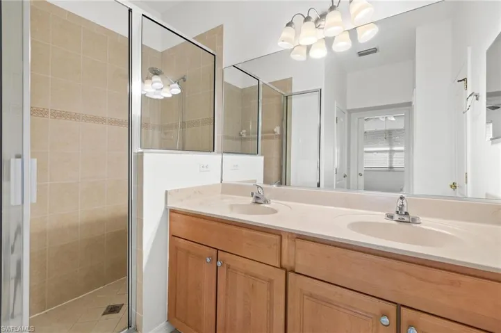 Full bathroom featuring a shower stall, double vanity, and a chandelier