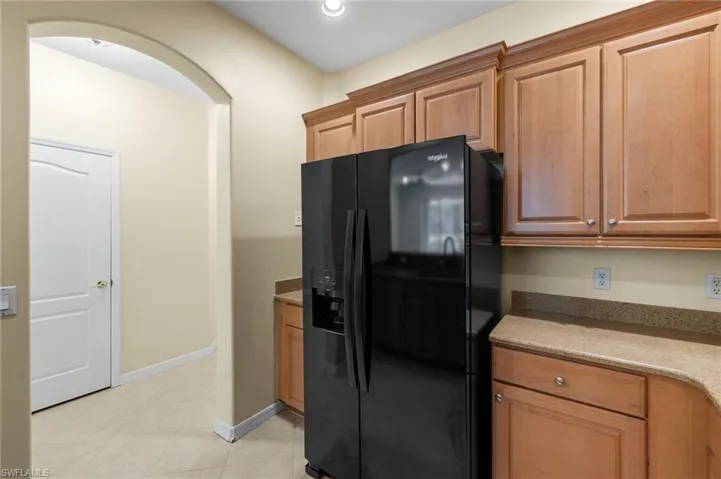Kitchen featuring black fridge, light stone countertops, brown cabinets, and recessed lighting