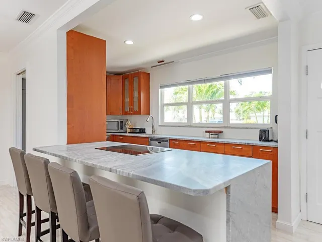 Kitchen with crown molding, light stone countertops, a breakfast bar area, brown cabinetry, and glass insert cabinets