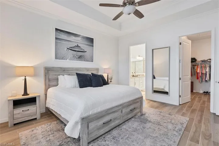 Bedroom with ensuite bathroom, a spacious closet, ceiling fan, a tray ceiling, and crown molding