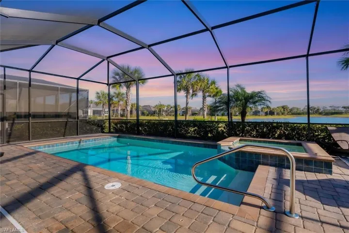 Pool at dusk with an in ground hot tub, a water view, glass enclosure, and a patio area