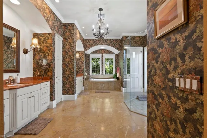 Full bathroom featuring vanity, a garden tub, a chandelier, crown molding, and a shower stall