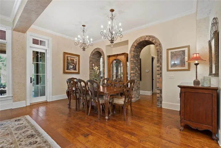 Dining area with crown molding, dark wood-type flooring, arched walkways, and a chandelier