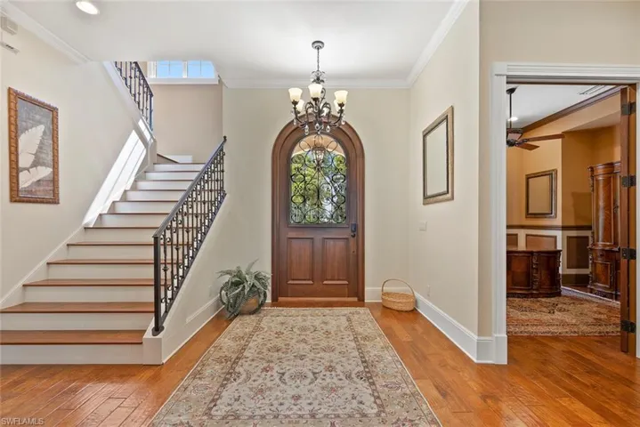 Foyer with crown molding, light wood-style flooring, a chandelier, ceiling fan, and stairway
