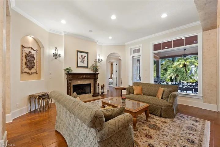 Living room with crown molding, a fireplace with flush hearth, arched walkways, dark wood-style floors, and recessed lighting