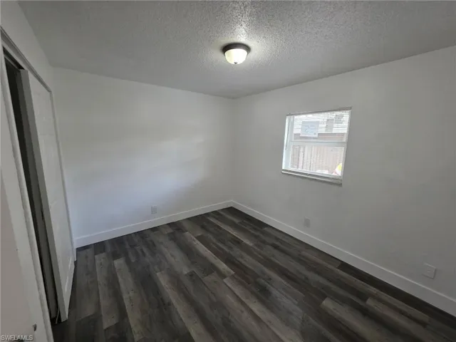 Unfurnished bedroom with a textured ceiling, dark wood finished floors, and a closet
