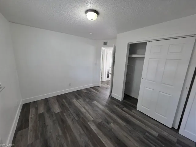 Unfurnished bedroom featuring a textured ceiling, a closet, and dark wood finished floors